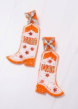 Load image into Gallery viewer, Game Day orange and white beaded earrings.  Each earring is shaped like a cowboy boot and is beaded with orange and white beads, five sequin stars, and star accents on the posts.  One earring says game and the other say day.